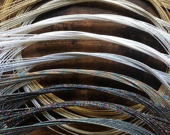 May include: A collection of metallic cords in various colours, including gold, silver, and iridescent. The cords are arranged in a circular pattern, with the gold cord at the top and the iridescent cord at the bottom.