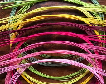 May include: A collection of colourful, thin, flexible wires arranged in a rainbow pattern, forming concentric circles on a wooden surface.