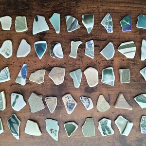 以下が含まれることがあります： 木製の表面に配置された、緑、青、ベージュの色合いの不規則な形の陶器の破片のコレクション。 破片のサイズとパターンは異なり、花柄やストライプのデザインが施されたものもあります。 全体的な美しさは素朴で芸術的です。