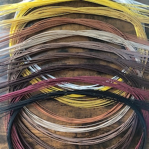Puede incluir: Una colección de alambre artesanal colorido en varios tonos, incluyendo dorado, plateado, cobre y negro. Los alambres están dispuestos en haces circulares sueltos, mostrando su flexibilidad y brillo metálico. Ideal para la creación de joyas y otros proyectos de manualidades.
