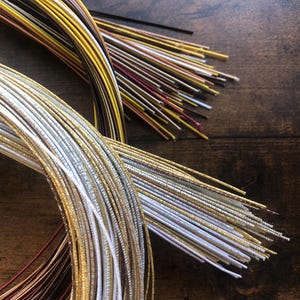 Peut inclure: Gros plan sur une variété de cordons métalliques de couleur or, argent, blanc et marron. Les cordons sont disposés en cercle sur une surface en bois.