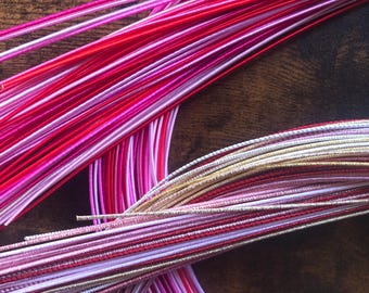 May include: A bundle of colourful satin cords in shades of pink, red, and white. The cords are arranged in a circular pattern, with some of the cords overlapping.