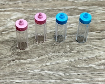 May include: Four small, clear plastic bottles with colorful lids. Two bottles have pink lids, and two have blue lids. The bottles are arranged on a wooden surface.