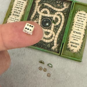 以下が含まれることがあります： 緑色のフレームと中央の道があるミニチュアボードゲーム。ADVENTURE A GAME FOR THOSE WHO SEEK TO FIND A WAY TO LEAVE THEIR WORLD BEHINDおよびBEWARE ITS JUNGLES CAN CHANGE WITHOUT WARNINGというテキストが書かれています。小さな白いサイコロが含まれています。