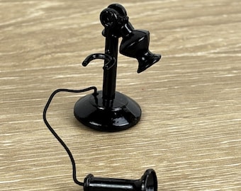 May include: A miniature black vintage telephone with a base, receiver, and cord. The receiver is detached, lying next to the base. The telephone is a decorative item, likely for a dollhouse or display.