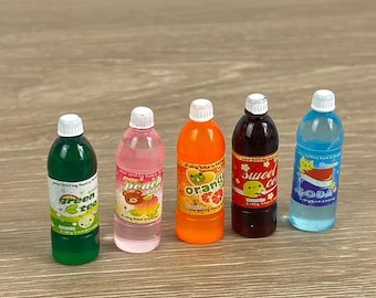 May include: Five miniature soda bottles with white caps and colorful labels. The bottles contain green tea, peach, orange, sweet cola, and soda. Each bottle has a different label design with fruit and cartoon characters.