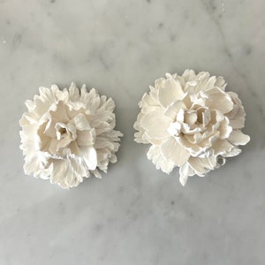 May include: Two white ceramic flower decorations, each with a detailed, layered design resembling a peony.