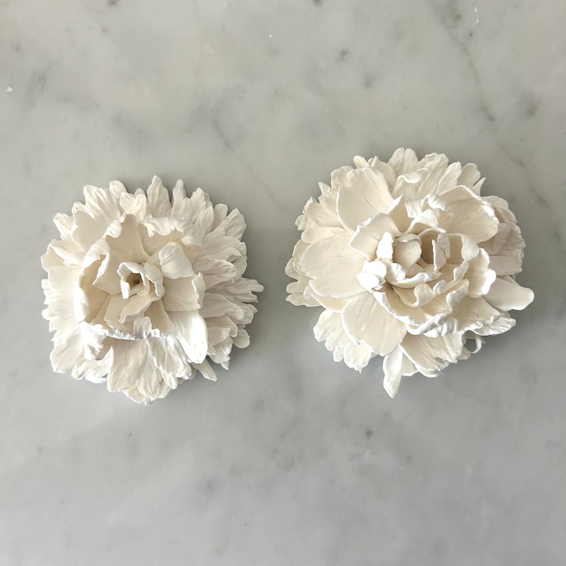 May include: Two white ceramic flower decorations, each with a detailed, layered design resembling a peony.