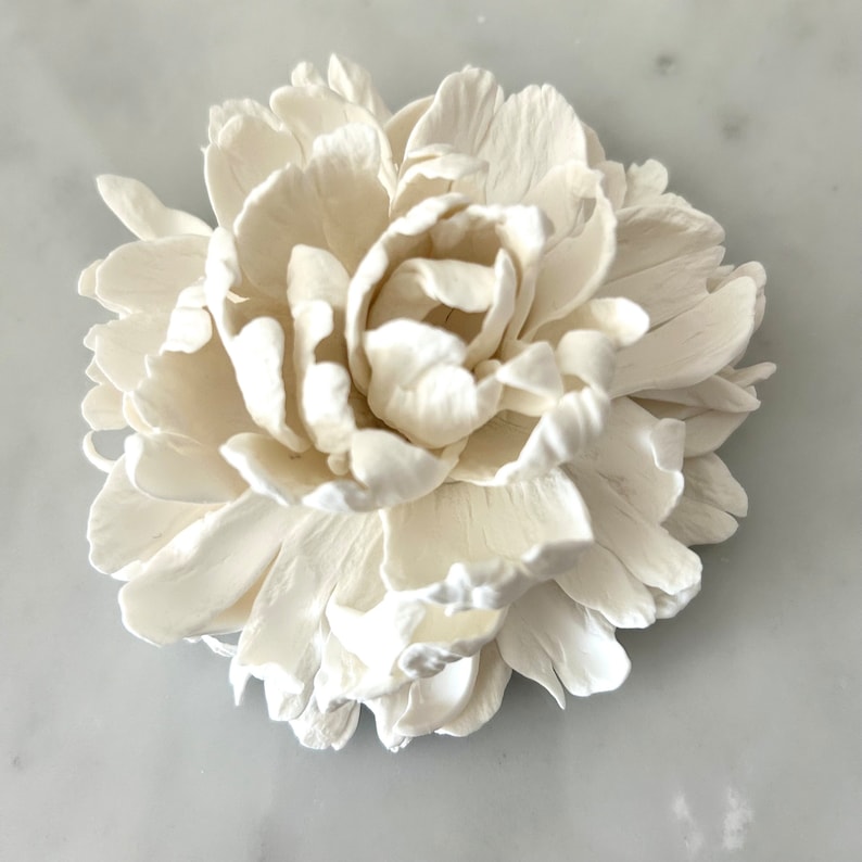May include: A white ceramic peony flower with a realistic design. The flower has multiple layers of petals and is a delicate and elegant decoration.