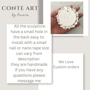 May include: White ceramic sculpture of a flower with a round center that has the initials "RC" on it. The sculpture has a small hole in the back for hanging.
