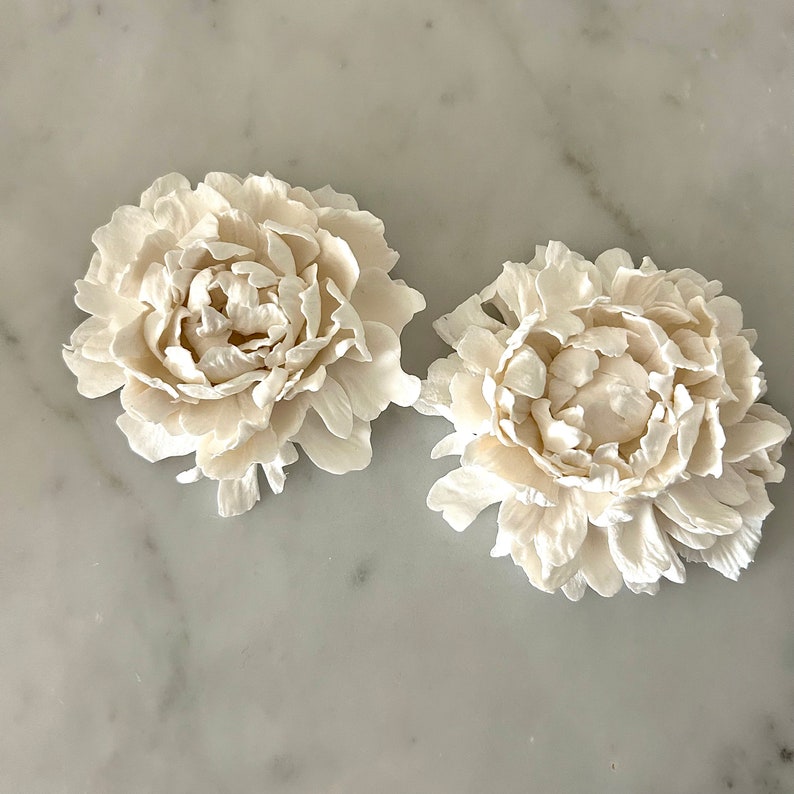 May include: Two white, ceramic peony flowers. The flowers are detailed and realistic.