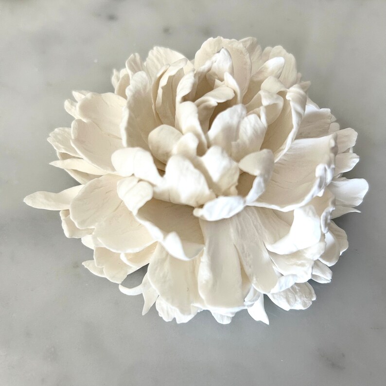 May include: A white ceramic peony flower. The flower is made of many petals and has a realistic appearance.