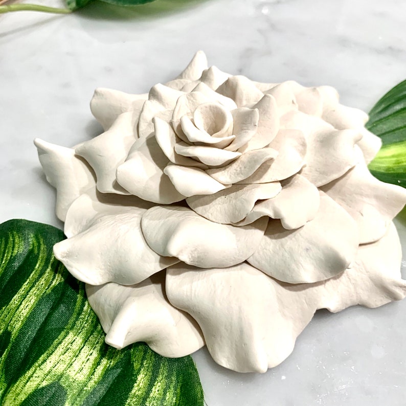Op de afbeelding: Een witte keramische gardenia-bloem met een gedetailleerd, realistisch ontwerp. De bloem is gemaakt van meerdere lagen bloemblaadjes, waardoor een driedimensionaal effect ontstaat.