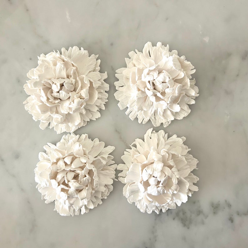May include: Four white ceramic peonies, each with a detailed, layered design, arranged in a square pattern on a white marble surface.