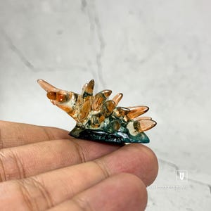 May include: A small, hand-blown glass sculpture of a sea creature with a spiky, orange-brown shell and a teal-coloured base.