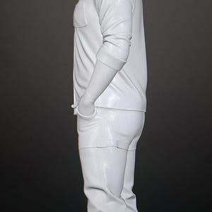 May include: A solid white figurine of a standing person in profile, wearing a collared button-down shirt with rolled sleeves, pants, and shoes. The figure has short hair and hands tucked into pockets, rendered in a smooth, monochromatic finish.