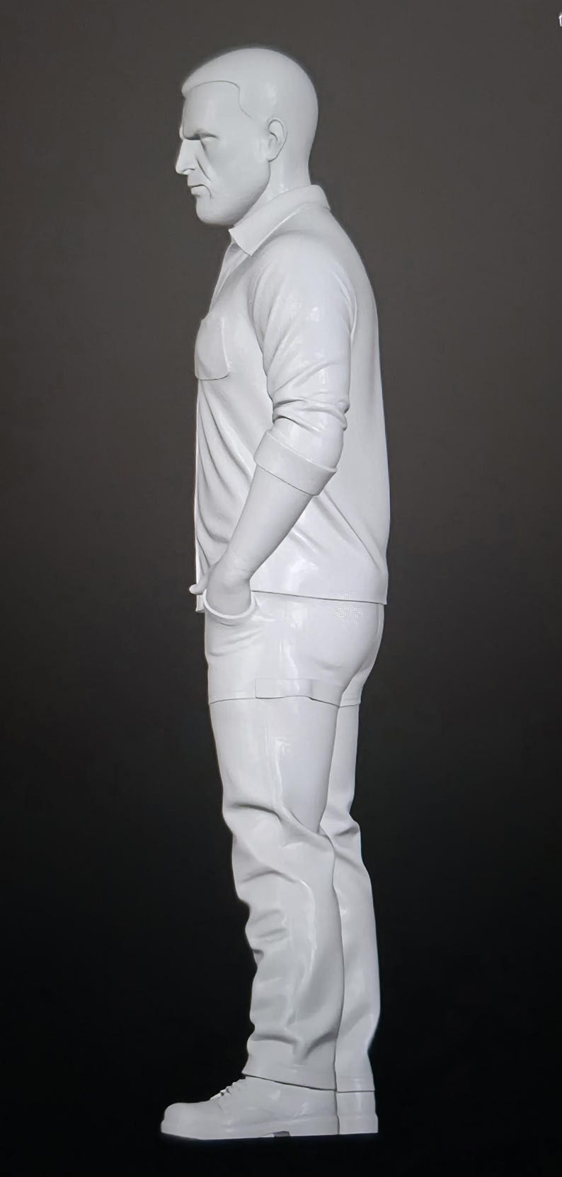 May include: A solid white figurine of a standing person in profile, wearing a collared button-down shirt with rolled sleeves, pants, and shoes. The figure has short hair and hands tucked into pockets, rendered in a smooth, monochromatic finish.