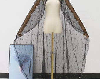 May include: Black sheer cape with a star pattern, displayed on a mannequin. The cape has a round neckline and a flowing design, with a multitude of small stars scattered across the fabric. The cape is floor-length and suitable for costumes or special events.