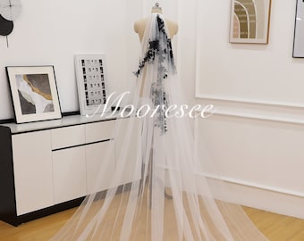 May include: A white tulle wedding veil with a black floral lace trim. The veil is long and flowing, and the lace trim is delicate and intricate.