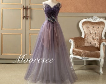 May include: A long, flowing purple tulle gown with a sweetheart neckline and a beaded embellishment at the waist. The gown has a gradient effect, fading from a darker purple at the top to a lighter purple at the bottom.