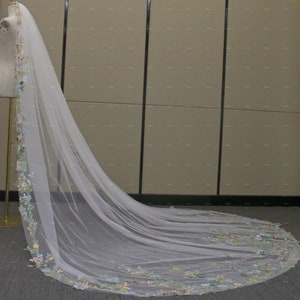 May include: A long, white tulle wedding veil with a floral embroidered border. The embroidery features colorful flowers in shades of pink, blue, and green.