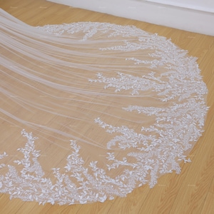 May include: A white bridal veil with a delicate floral lace pattern and beaded embellishments. The veil is made of soft tulle and has a scalloped edge.