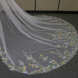 May include: A white tulle wedding veil with a floral embroidery design. The embroidery features pastel blue, pink, yellow, and green flowers.