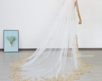 May include: A long white bridal veil with a gold lace trim. The veil is draped over a mannequin and the lace trim is visible at the bottom of the veil.