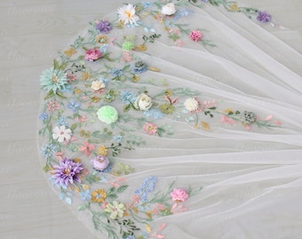May include: A white bridal veil with an intricate floral design. The veil is adorned with colorful, embroidered flowers in shades of pink, purple, blue, and yellow. The flowers are arranged along the edges of the veil, creating a delicate and romantic look.