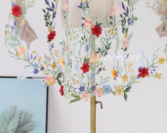 May include: White sheer fabric with colorful embroidered flowers. The flowers are red, yellow, blue, pink, and green. The fabric is on a gold stand.