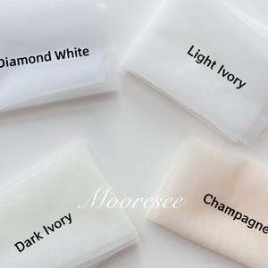 May include: Four fabric swatches in shades of white and ivory. The swatches are labeled "Diamond White", "Light Ivory", "Dark Ivory", and "Champagne". The fabric is a fine mesh, likely tulle, and is folded neatly. The word "Mooresee" is also visible.