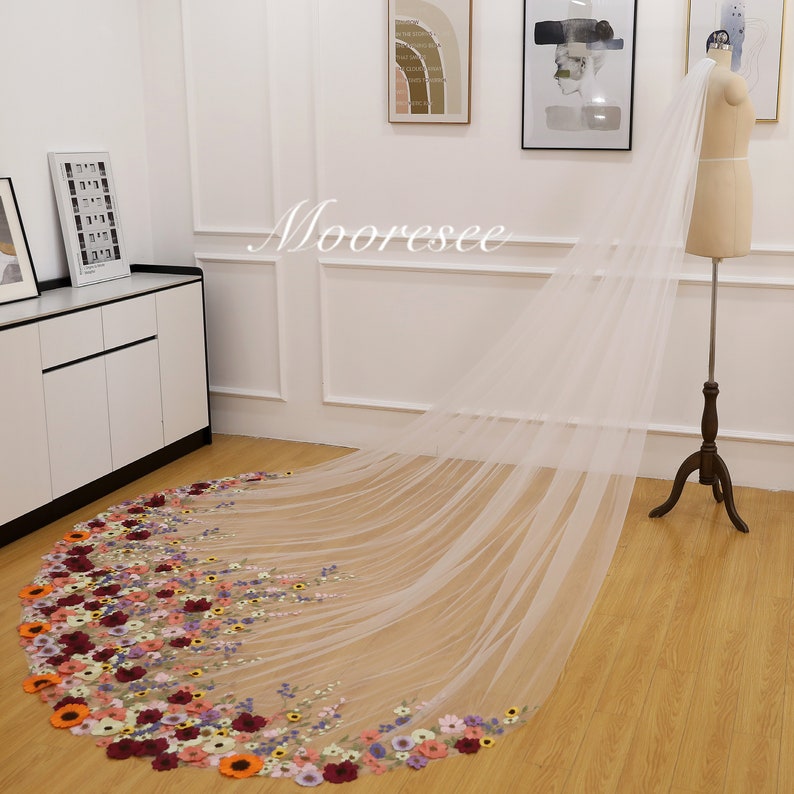 May include: A long white tulle wedding veil with a floral design. The veil is decorated with colorful embroidered flowers, including red, orange, yellow, pink, purple, and blue.