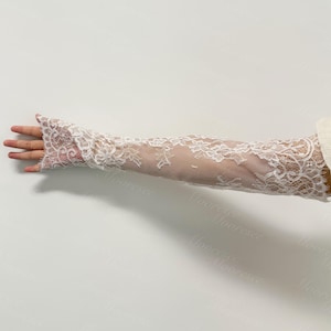 May include: White lace arm sleeves with floral patterns. The sleeves are long, covering the arm from the wrist to the upper arm. The lace is delicate and detailed, creating a romantic and elegant look. Ideal for weddings or special occasions.