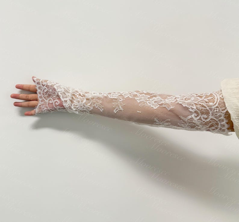 May include: White lace arm sleeves with floral patterns. The sleeves are long, covering the arm from the wrist to the upper arm. The lace is delicate and detailed, creating a romantic and elegant look. Ideal for weddings or special occasions.
