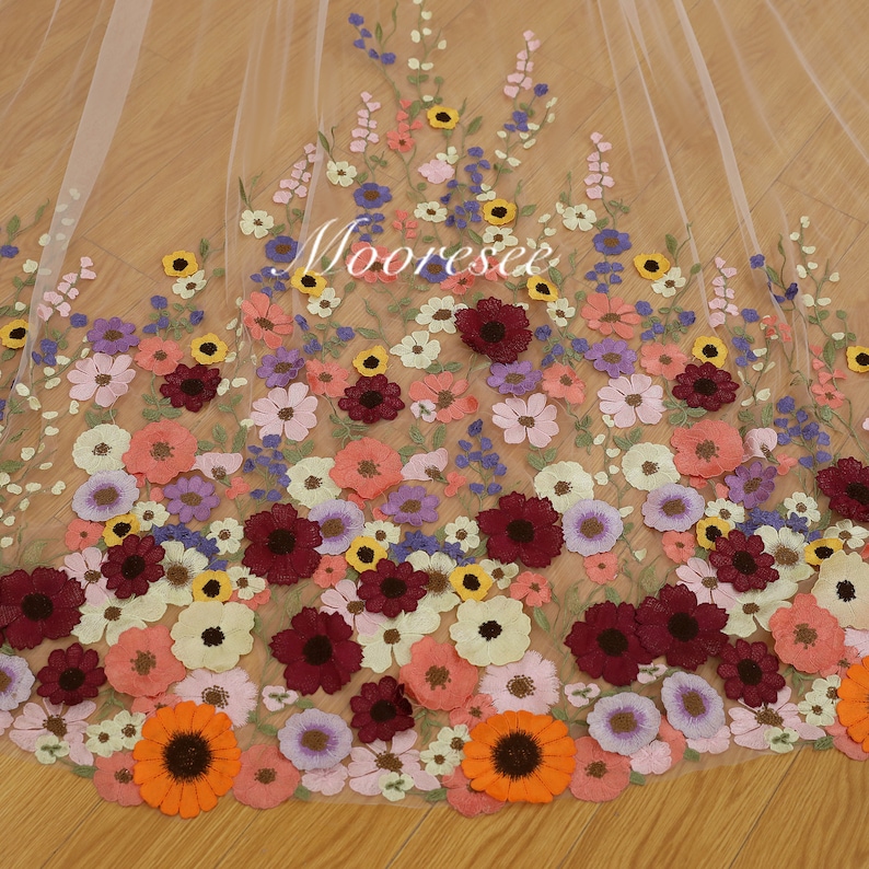 May include: A sheer white fabric with embroidered flowers in various colors, including red, pink, yellow, orange, and purple. The flowers are arranged in a cascading pattern, creating a delicate and romantic look.