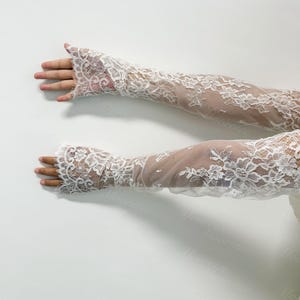 May include: A pair of white lace gloves with a floral pattern. The gloves are long, extending past the elbows, and feature a delicate, openwork design. The lace is detailed and intricate, creating a romantic and elegant appearance.