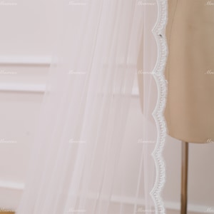 May include: A white bridal veil with a scalloped lace trim. The veil is made of soft tulle and is perfect for a wedding ceremony.