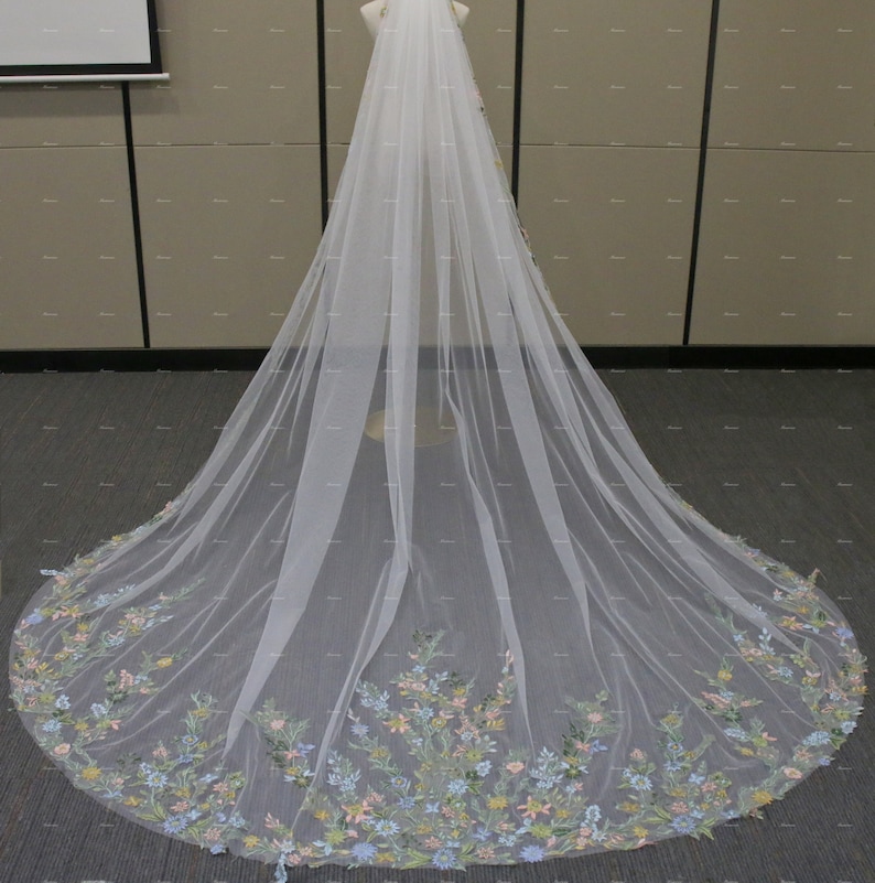 May include: A long white tulle wedding veil with a floral embroidered border in shades of blue, pink, and green.