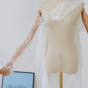 May include: A white lace bridal veil and matching lace sleeves are displayed on a mannequin. The veil is layered and sheer, with delicate lace detailing. The sleeves are long and fitted, with intricate floral lace patterns.