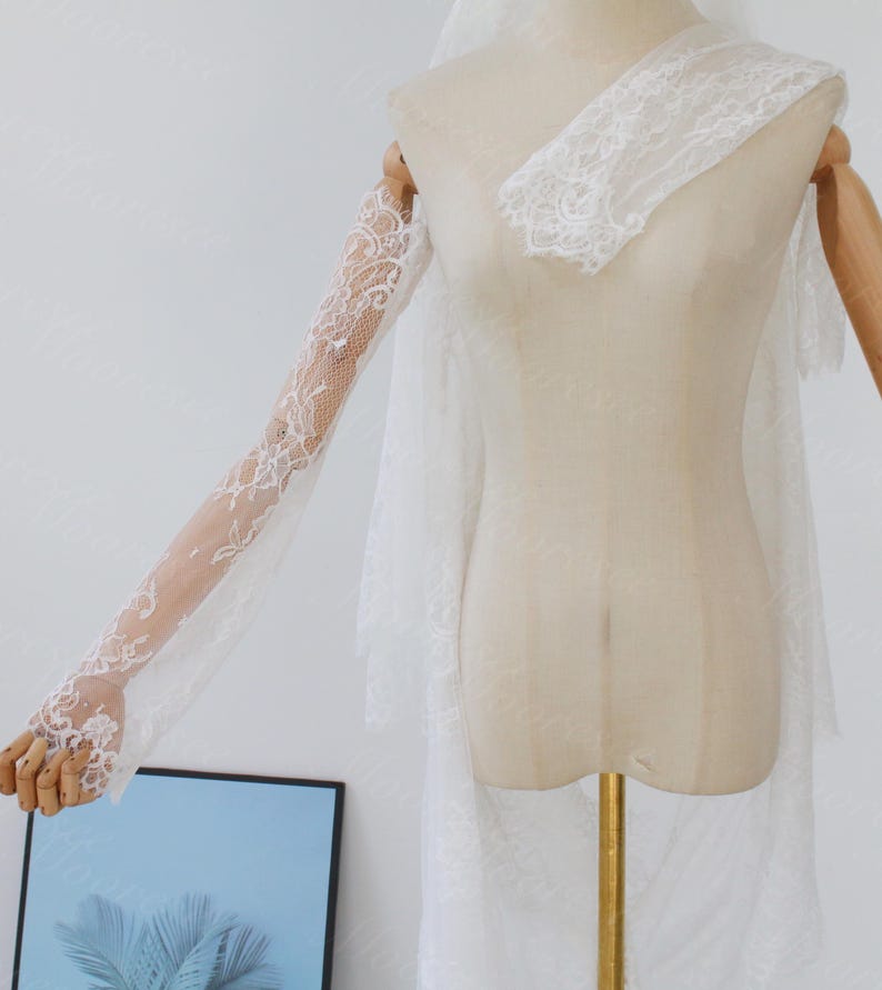May include: A white lace bridal veil and matching lace sleeves are displayed on a mannequin. The veil is layered and sheer, with delicate lace detailing. The sleeves are long and fitted, with intricate floral lace patterns.