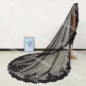 May include: A long, black bridal veil with intricate lace detailing along the edges. The veil is displayed on a mannequin, showcasing its flowing design and delicate floral patterns. The veil's length extends to the floor, creating a dramatic effect.