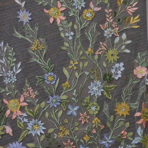 May include: A close-up of a delicate floral fabric with a repeating pattern of embroidered flowers in shades of pink, blue, yellow, and green. The fabric has a sheer, almost translucent quality.