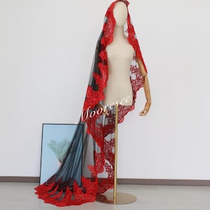 May include: A black tulle veil with a red lace trim. The veil is draped over a mannequin and is long enough to reach the floor.