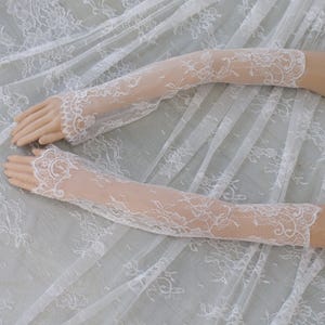 May include: A pair of white lace gloves with a floral design. The gloves are long, reaching past the elbows, and are made of delicate, openwork lace. The intricate floral patterns add an elegant and romantic touch to the gloves.