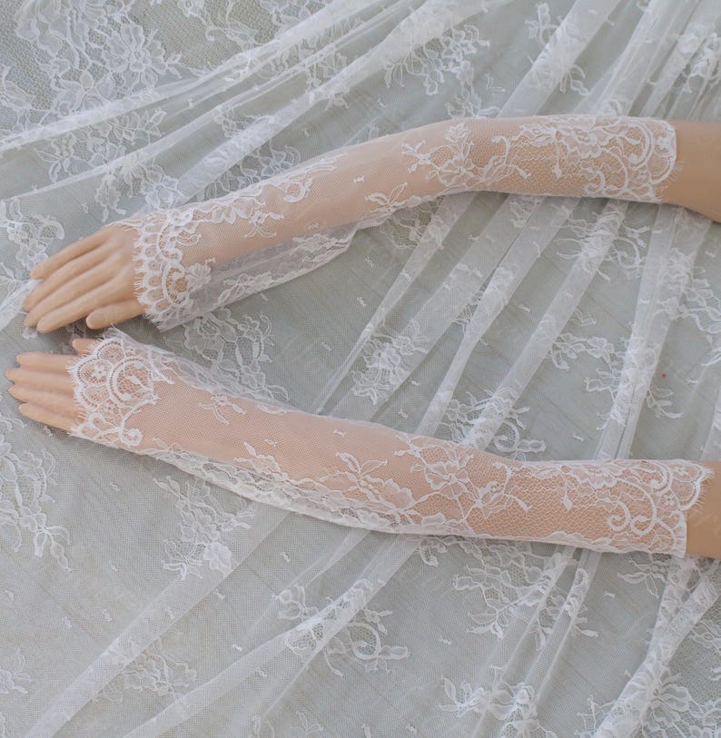 May include: A pair of white lace gloves with a floral design. The gloves are long, reaching past the elbows, and are made of delicate, openwork lace. The intricate floral patterns add an elegant and romantic touch to the gloves.