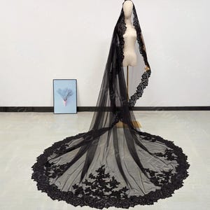 May include: A black bridal veil with intricate lace detailing. The veil is displayed on a mannequin, showcasing its full length and delicate design. The lace trim adds a touch of elegance to the sheer fabric.