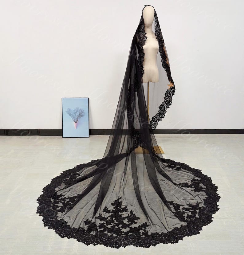 May include: A black bridal veil with intricate lace detailing. The veil is displayed on a mannequin, showcasing its full length and delicate design. The lace trim adds a touch of elegance to the sheer fabric.