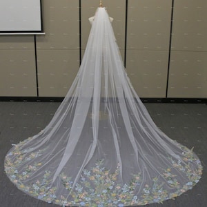 May include: A white bridal veil with a floral embroidered border. The embroidery features pastel pink, blue, and green flowers.