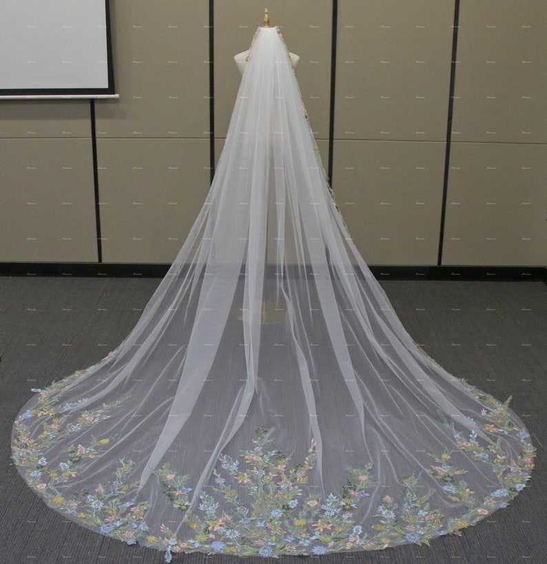 May include: A white bridal veil with a floral embroidered border. The embroidery features pastel pink, blue, and green flowers.