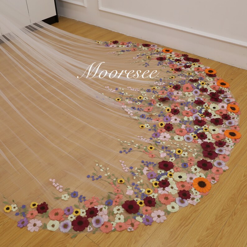 May include: A white tulle wedding veil with a floral design. The veil is decorated with colorful embroidered flowers, including pink, purple, yellow, orange, and red.